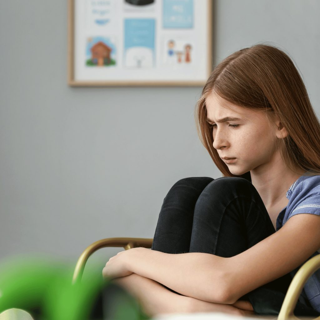 Teenage girl sitting with knees hugged close.