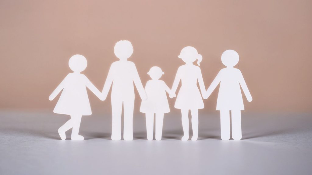 Paper‑cut style silhouettes of five people—two adults and three children—standing in a row and holding hands against a soft beige background.
